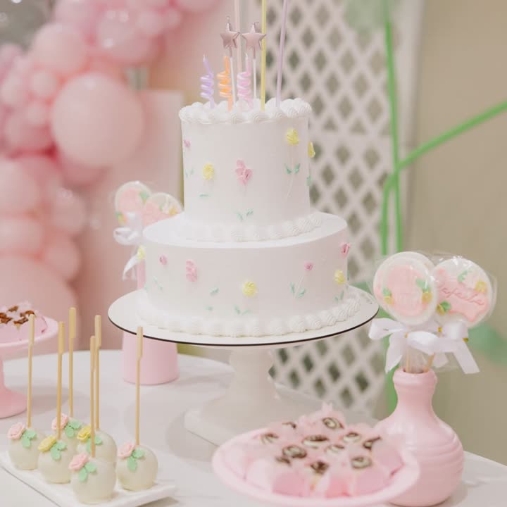 Bolo branco de dois andares decorado com flores delicadas em tons pastel e velas coloridas