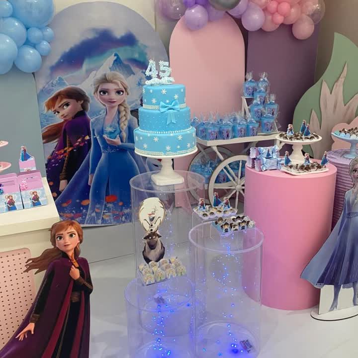 Decoração temática Frozen com bolo azul, Elsa e Anna, e balões em tons de lilás e rosa